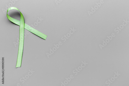 Green ribbon for Lyme disease, kidney cancer, organ donation awareness on grey background top view copyspace