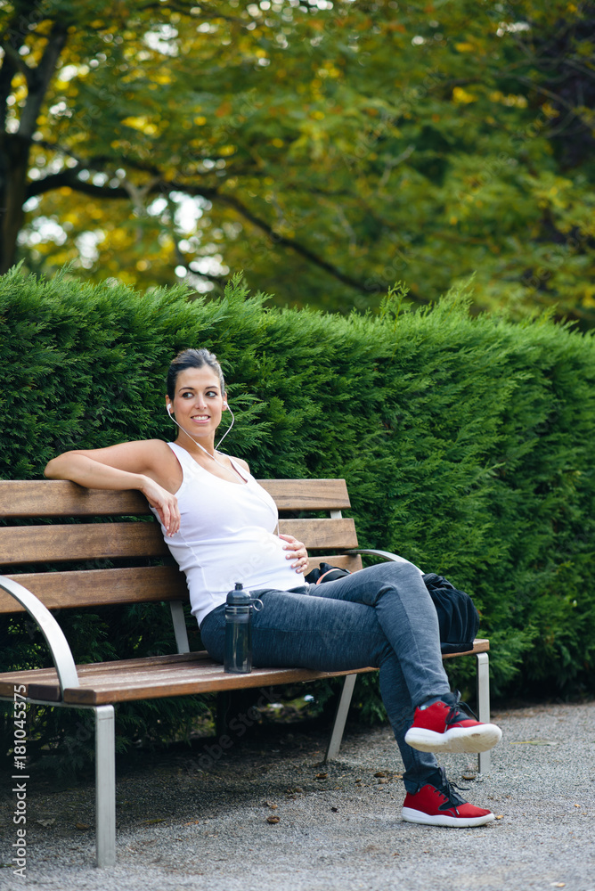 Relaxed sporty pregnant woman sitting in a park bench for resting after outdoor healthy fitness workout. Relaxed sporty pregnant woman sitting in a park bench for resting after outdoor healthy fitness workout.