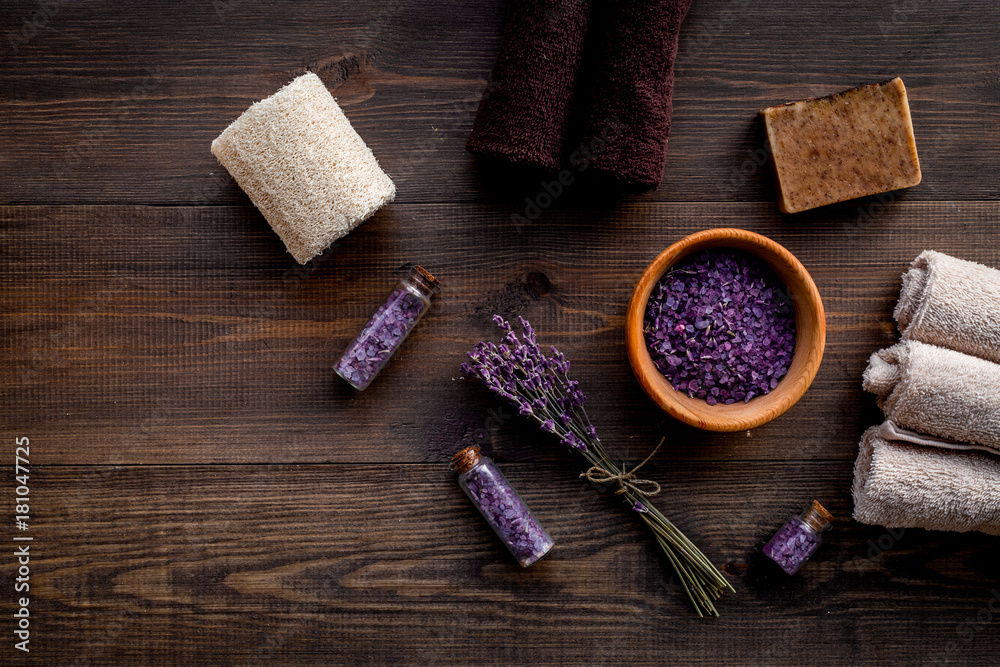 Floral foot spa with lavender. Spa salt, sponge, soap, towel on dark wooden background top view copyspace Floral foot spa with lavender. Spa salt, sponge, soap, towel on dark wooden background top view copyspace