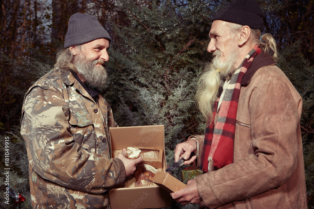 Two homeless older men celebrating christmas in park with gifts