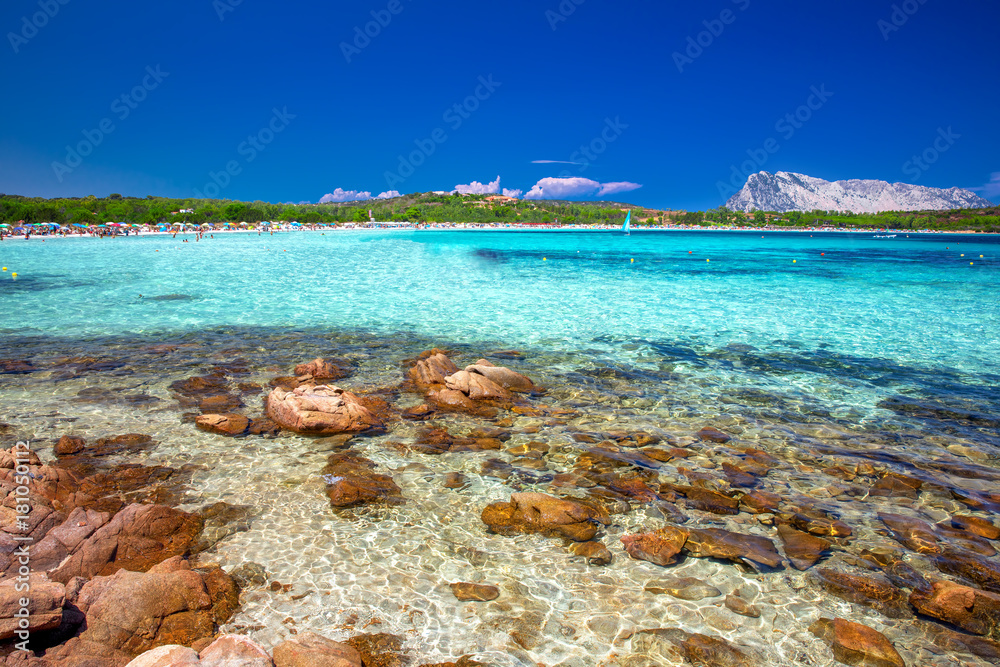 Lu Impostu beach with Isola Travolara in the background, red stones and azure clear water, San Teodoro, Sardinia, Italy