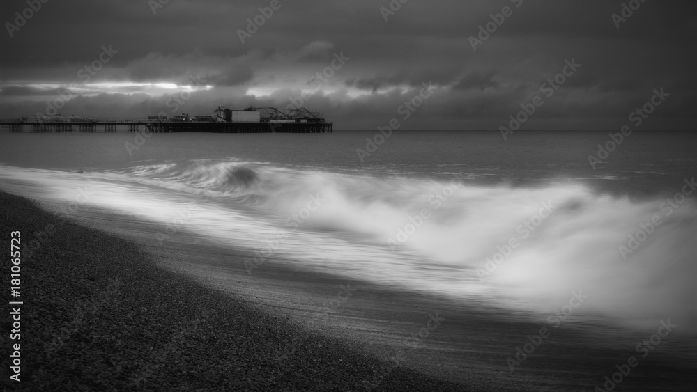 Long Exposure Black & White Image of Palace Pier, Brighton, UK with Wave Breaking Against the Shore in the Foreground 