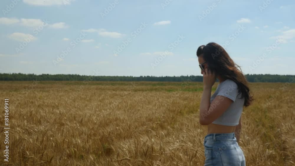 Long-haired woman talks on smartphone while walking on goldish wheatfield Long-haired woman talks on smartphone while walking on goldish wheatfield