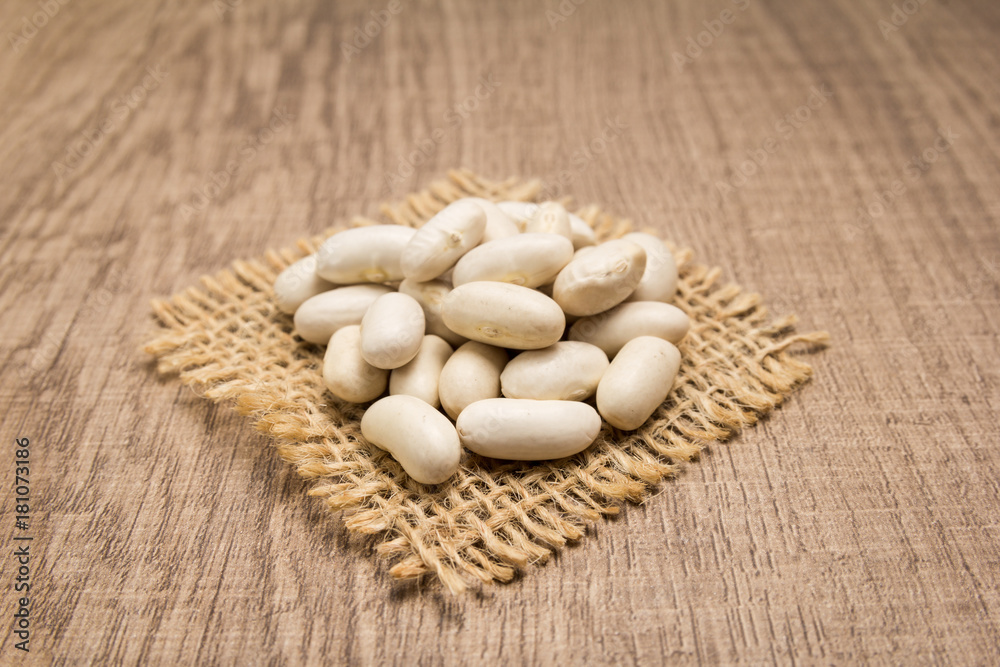 Navy Bean legume. Grains on square cutout of jute. Wooden table. Selective focus.