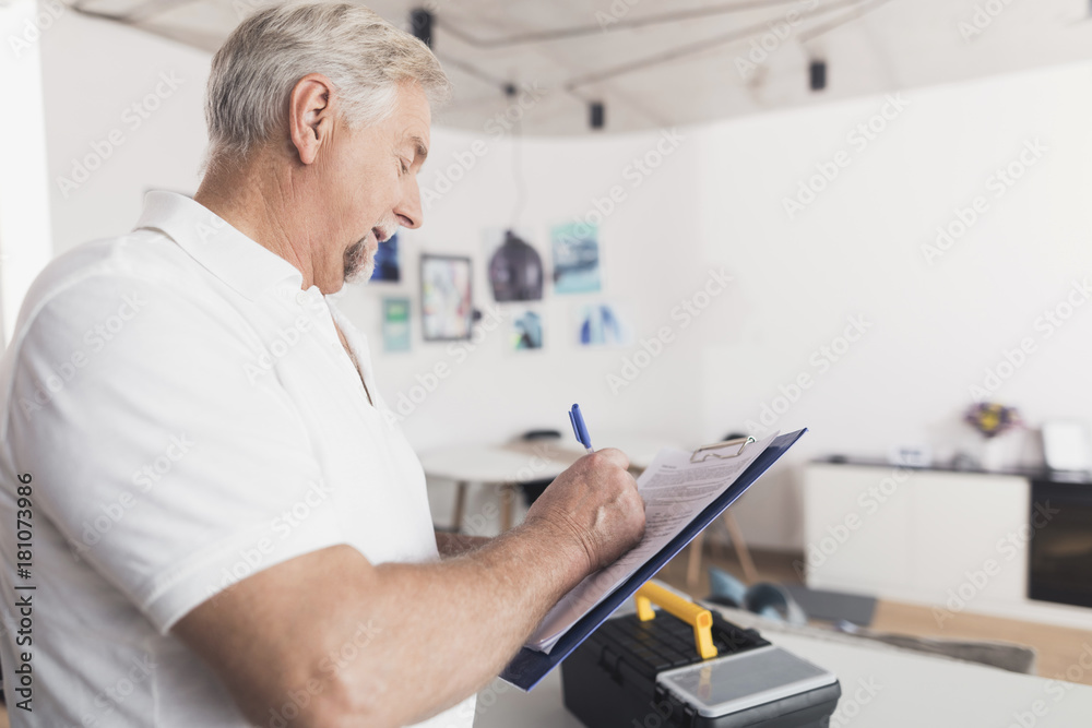 The man is in the kitchen. He holds a form for papers in his hands. Next to him stands a black box for the instrument. The man is in the kitchen. He holds a form for papers in his hands. Next to him stands a black box for the instrument.