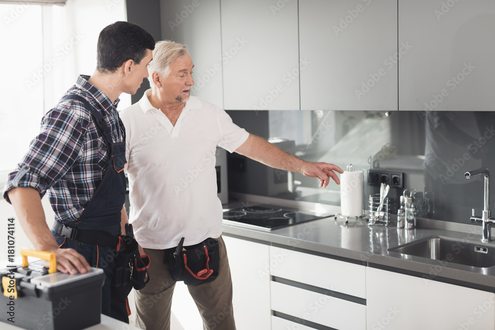 Two men of plumbers are standing in the kitchen and inspecting the future site for repair work. Two men of plumbers are standing in the kitchen and inspecting the future site for repair work.