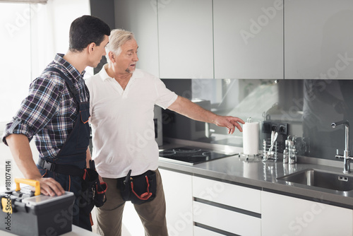 Two men of plumbers are standing in the kitchen and inspecting the future site for repair work.