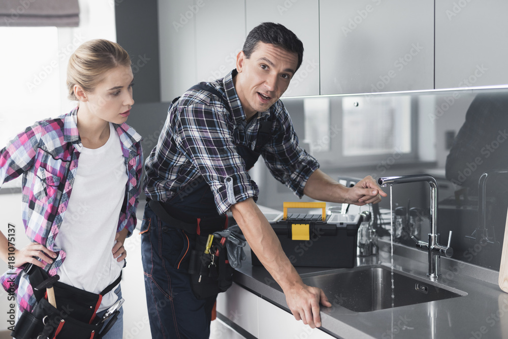 Obraz premium A man and a woman plumber repair a kitchen faucet from the client at home.