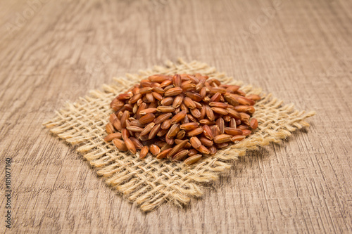 Bhutanese Red Rice seed. Grains on square cutout of jute. Wooden table. Selective focus.