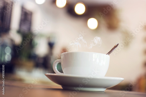 White cup with steaming hot coffee on table with bokeh background at coffee shop