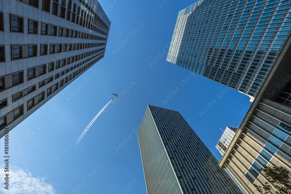 Tall city buildings and a plane flying overhead.