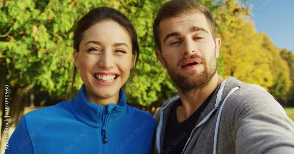 Close up of young smiling sporty couple videochatting and showing their thumbs up in the sunny park in early fall. Outside. Portrait. POV Close up of young smiling sporty couple videochatting and showing their thumbs up in the sunny park in early fall. Outside. Portrait. POV