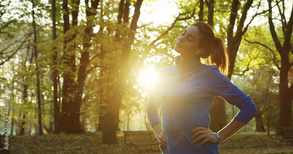 Young woman runner stretching her neck before jogging early in the morning in the beautiful green park. Outdoors