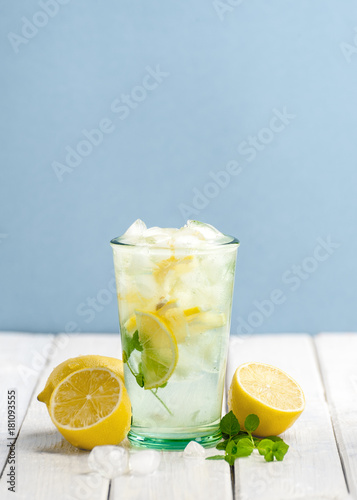 Cold lemonade and fresh lemons on a white wooden table on a blue background..
