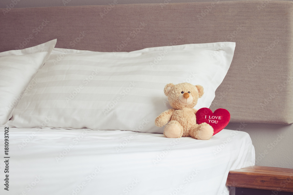 Cute little teddy bear sitting alone with hearts shape doll on white bed in morning. love romantic concept.
