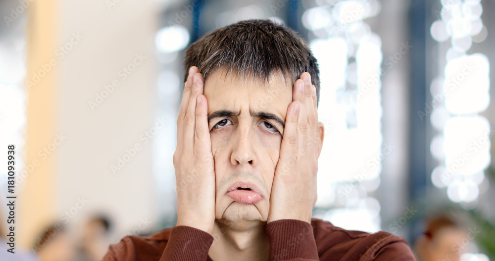 The guy clamps his face with his hands making a funny sad face in a public  place looks at camera in the interior. Stock Photo | Adobe Stock