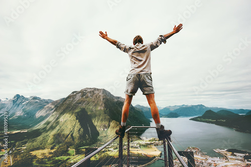 Man raised hands balancing at the edge cliff Rampestreken landmark in Norway mountains Travel lifestyle risk concept active vacations happy tourist enjoying landscape aerial view