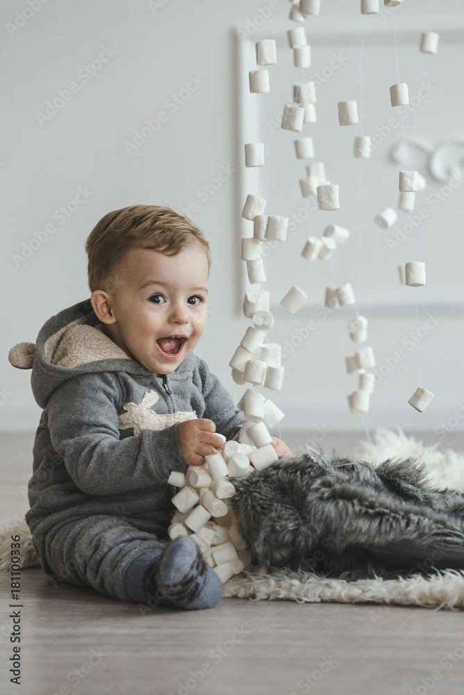 Little boy in grey pyjamas sits on the floor and play with marshmallow garland Little boy in grey pyjamas sits on the floor and play with marshmallow garland