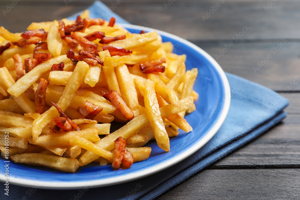 Plate with French fries and bacon on wooden table