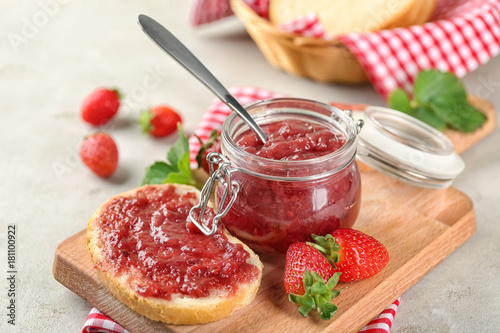 Jar and piece of bread with strawberry jam on table