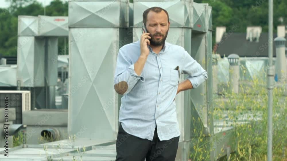 Young man with cellphone checking air conditioning on roof
Young man with cellphone checking air conditioning on roof