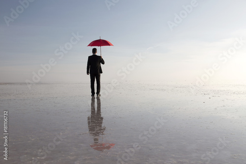 Businessman in black suit with a red umbrella on salt lake