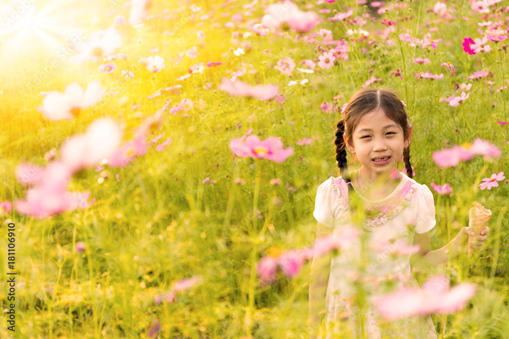 Cute little girl eating ice cream in the field of pink flowers at sunlight Cute little girl eating ice cream in the field of pink flowers at sunlight