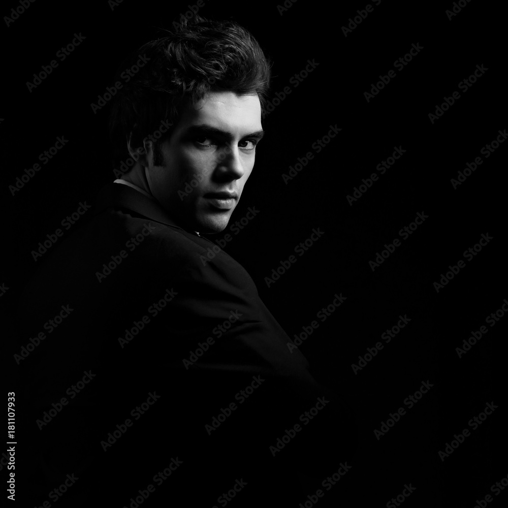 Fototapeta premium Handsome charismatic man looking serious in dark shadow dramatic light. Black and white portrait. Art