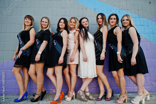 Group of 8 girls wear on black and 2 brides at hen party against colourful wall.