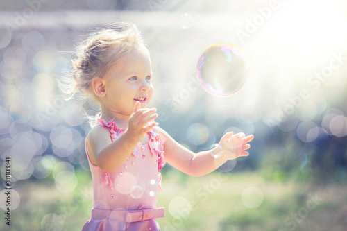 A little girl catches soap bubbles in summer park