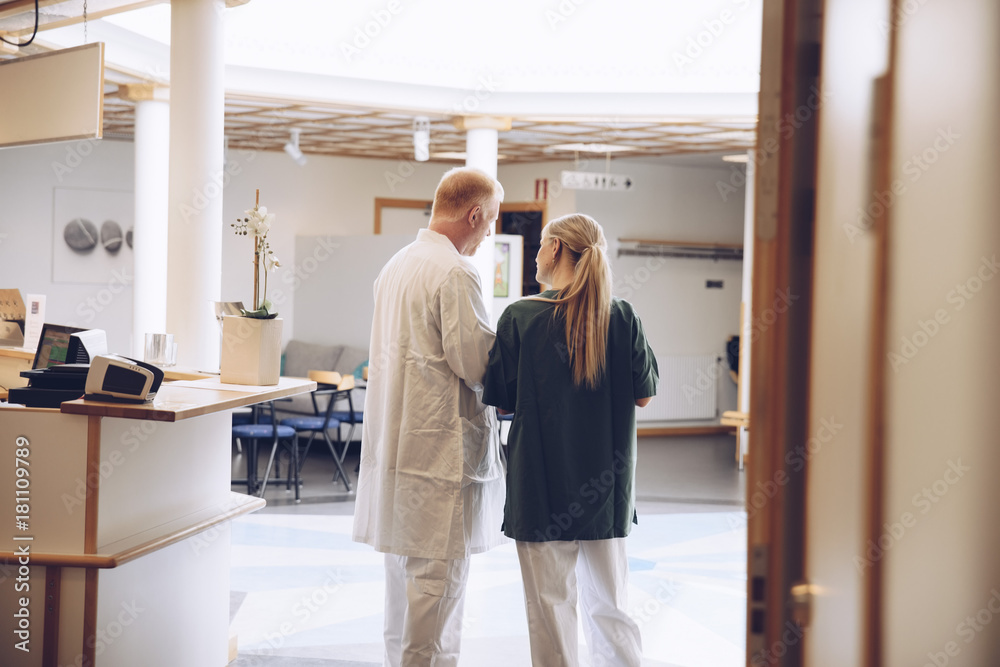 Rear view of female nurse and male doctor discussing while standing in hospital lobby Rear view of female nurse and male doctor discussing while standing in hospital lobby