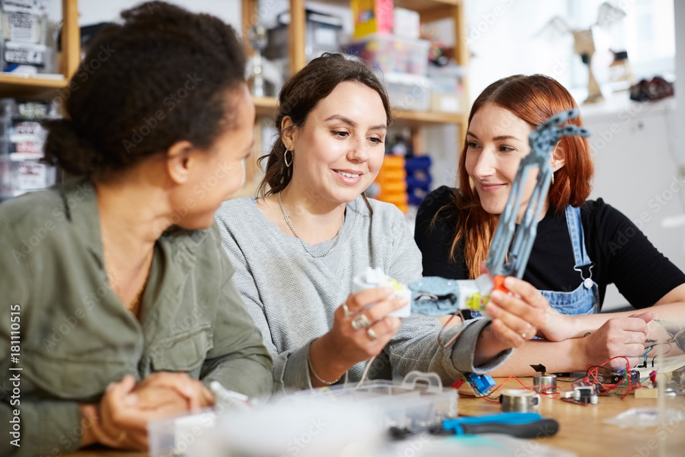 Smiling female inventors sitting with robot model at table in workshop