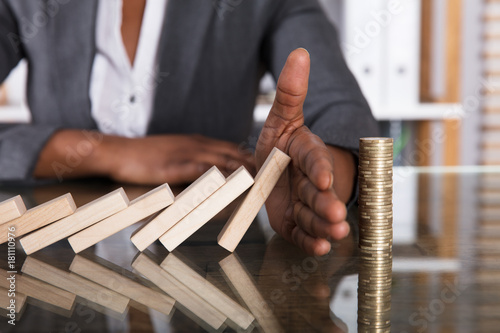 Human Hand Stopping Wooden Blocks From Falling On Stacked Coins