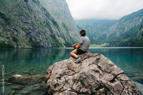 Girl sitting on rock looking at beautiful and misty lake in the