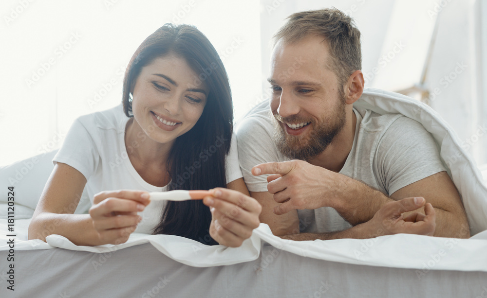 Good news. Handsome man expressing positivity and lying near his girlfriend while pointing at stripe Good news. Handsome man expressing positivity and lying near his girlfriend while pointing at stripe