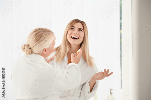 Mature woman with daughter using cosmetic products in bathroom