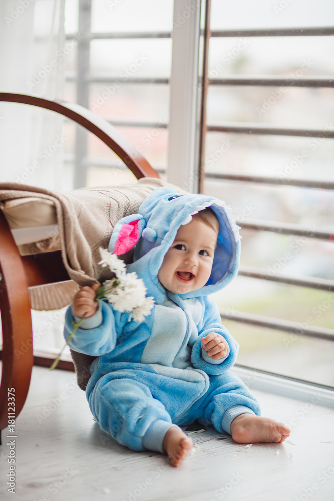 Little baby in blue suit looks like a Stitch sitting on the floor before bright window Little baby in blue suit looks like a Stitch sitting on the floor before bright window