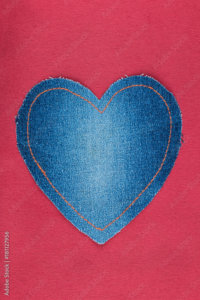 Heart made of denim lies on a red satin. Space for text.
