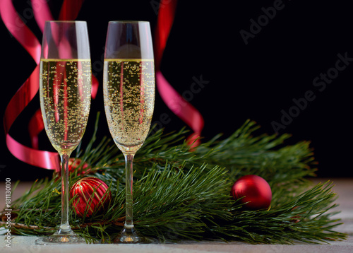 A couple of glasses with champagne on a white wooden table with Christmas balls