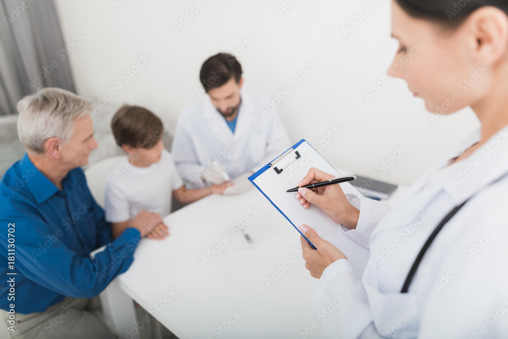 The doctor in white gloves takes a blood sample from the boy's finger. A nurse is making notes on the form. The doctor in white gloves takes a blood sample from the boy's finger. A nurse is making notes on the form.