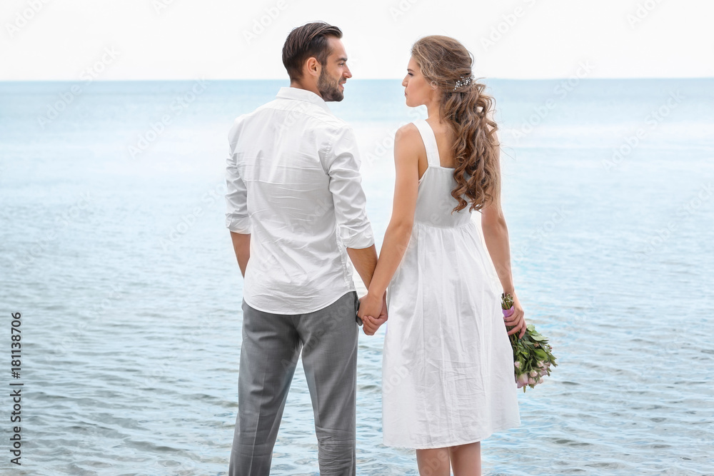 Happy newlywed couple standing on seashore
