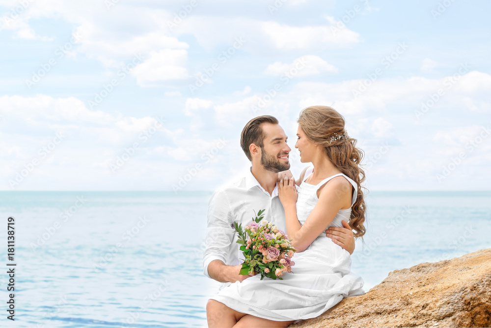 Happy newlywed couple sitting on rocky beach