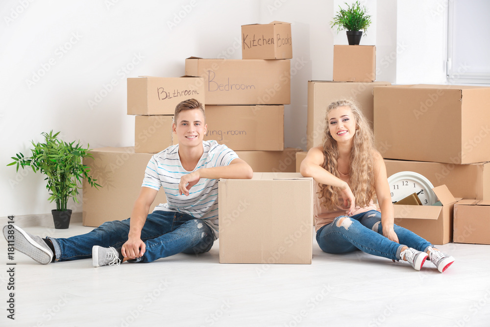 Young couple with moving boxes on floor in room - obrazy, fototapety, plakaty 