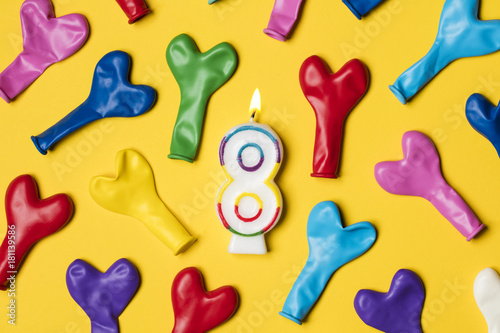 Number 8 candle with party balloons on a bright yellow background