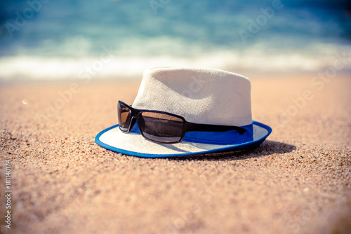 Beach hat and sunglasses lying on the sand by the sea 