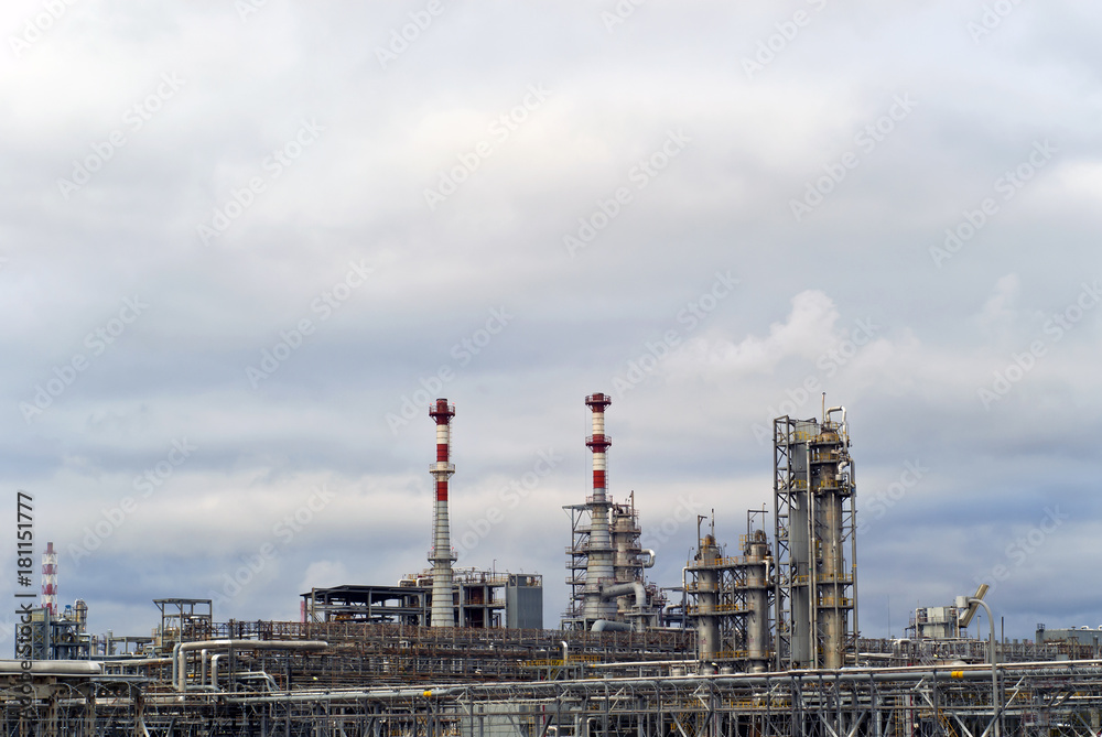 general view of a chemical or oil refinery with a multitude of pipelines, factory pipes and distillation columns under a cloudy sky