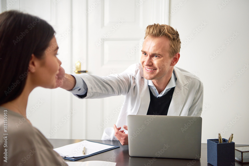 Male cosmetologist touching woman face at laptop during consultation Male cosmetologist touching woman face at laptop during consultation