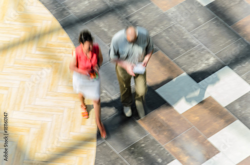 Silhouettes of Two Walking People in the Atrium of a Large Public Building, View from Above. Blur in Motion, Long Exposure. Abstract Background