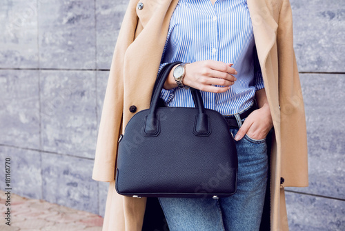 Trendy woman in beige coat and jeans with black big bag