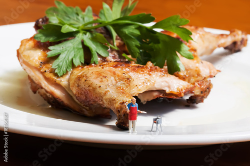 Barbeque party concept. Miniature figure cook against big grilled bbq chicken on a white plate.